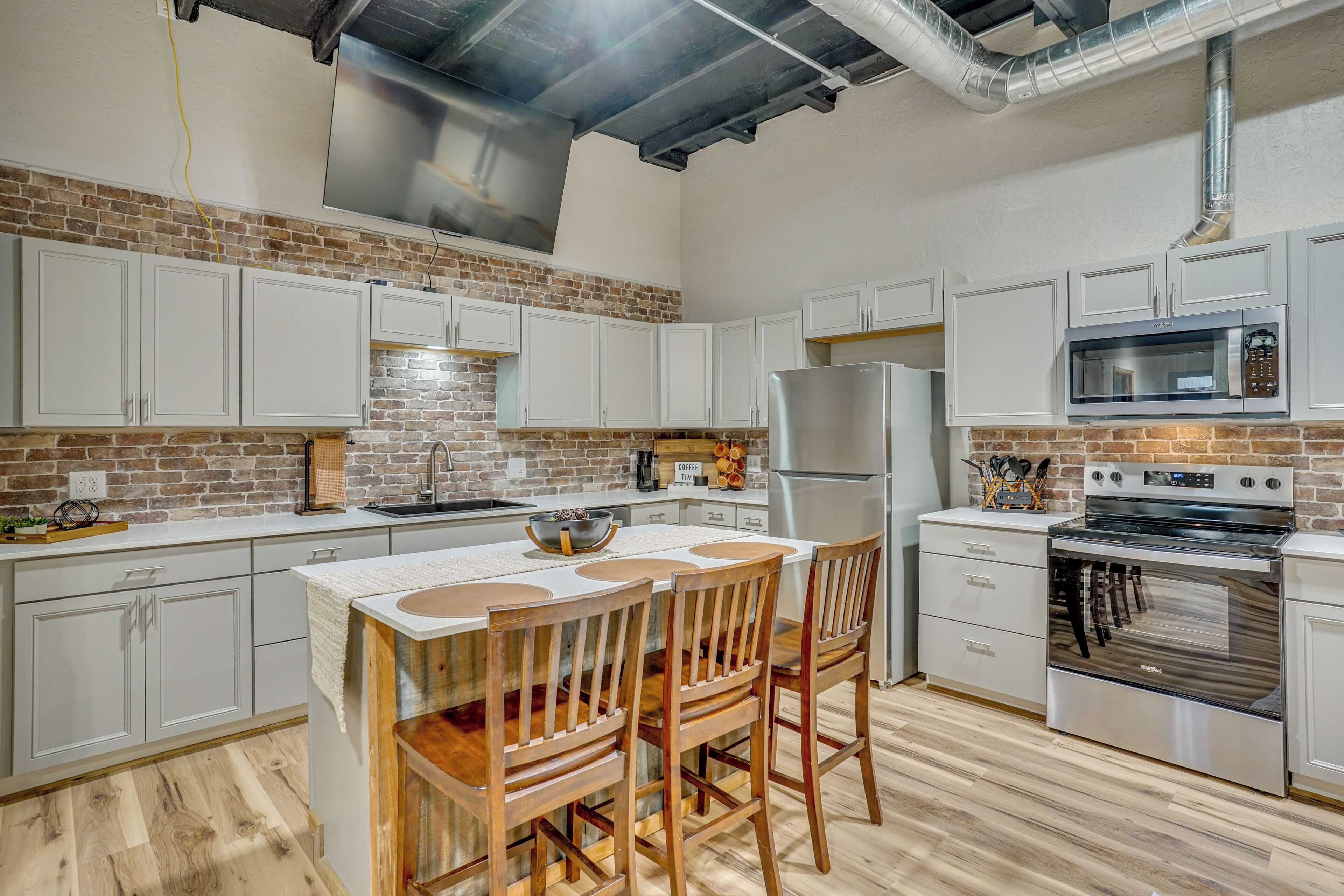 A kitchen with white cabinets, a brick wall, a stainless steel refrigerator, a microwave, and a stove.