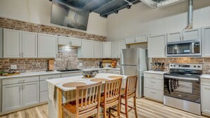 Una cocina con armarios blancos, pared de ladrillo, refrigerador de acero inoxidable, microondas y estufa.