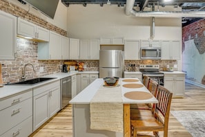 A modern kitchen with white cabinets, a stainless steel refrigerator, a microwave, and a dining area with a table and chairs.