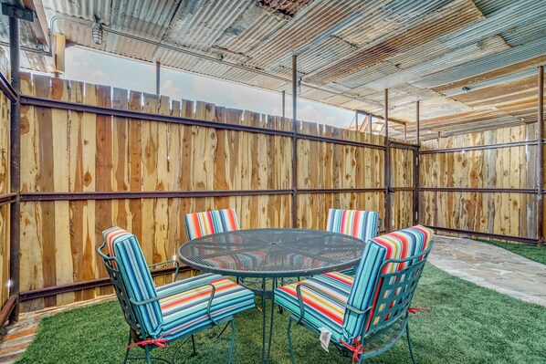 A covered patio with a round table and striped chairs, surrounded by a wooden fence.