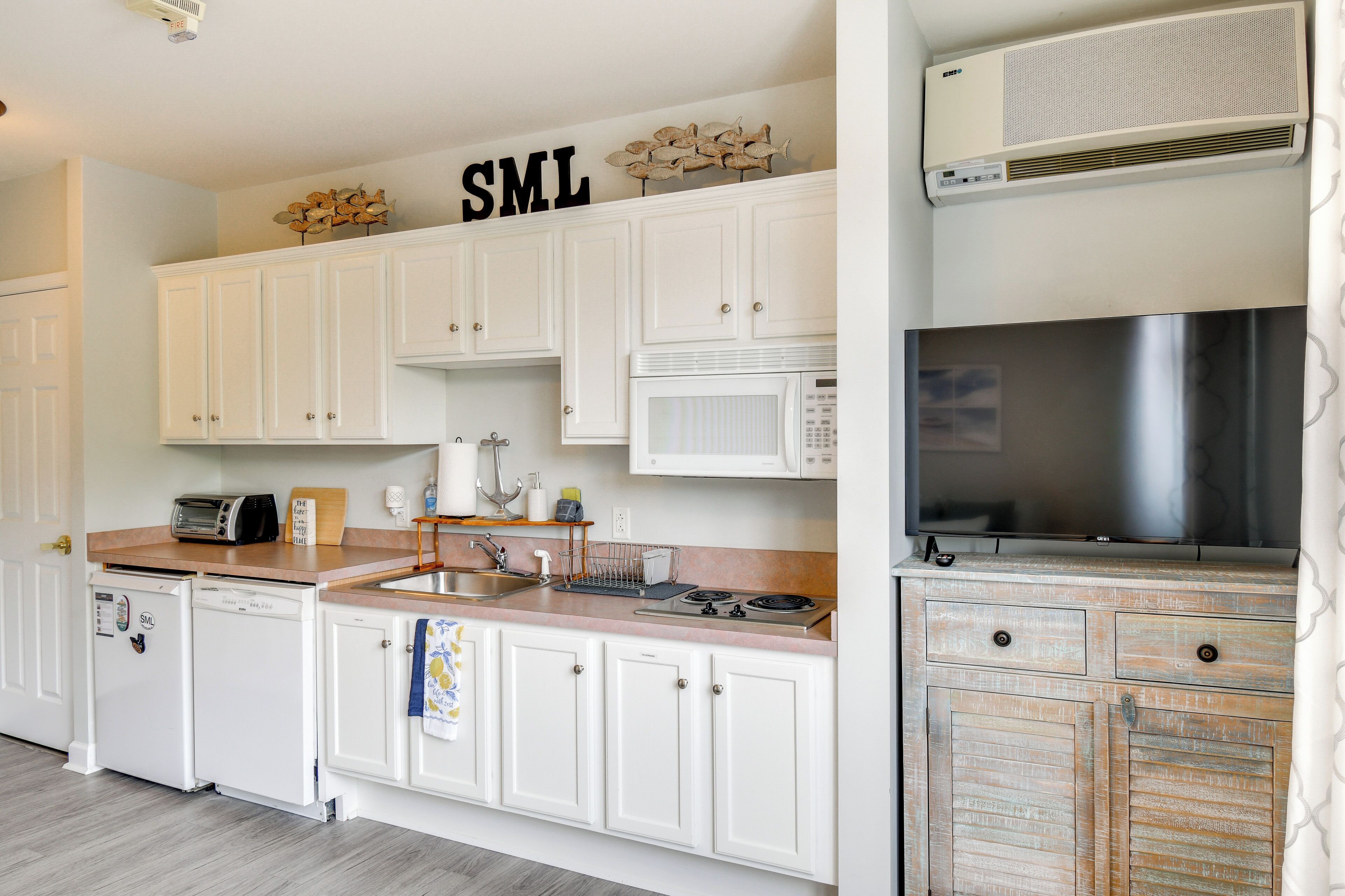 A kitchen with white cabinets, a microwave, a toaster, a sink, and a stainless steel range hood.
