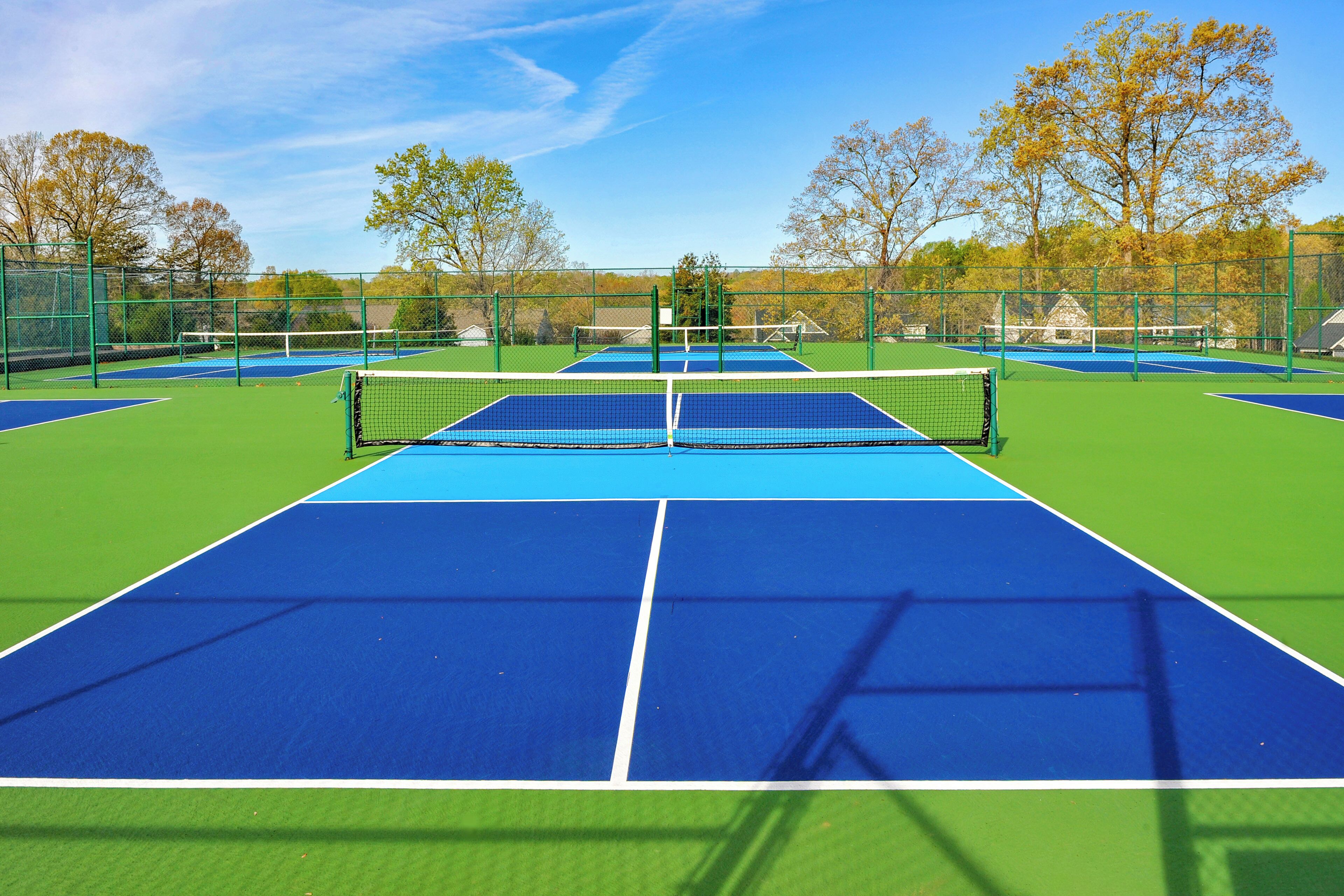 A tennis court with a net, surrounded by a fence, and trees in the background.