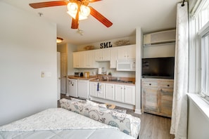 A bedroom with a bed, a ceiling fan, and a kitchenette with white cabinets and appliances.