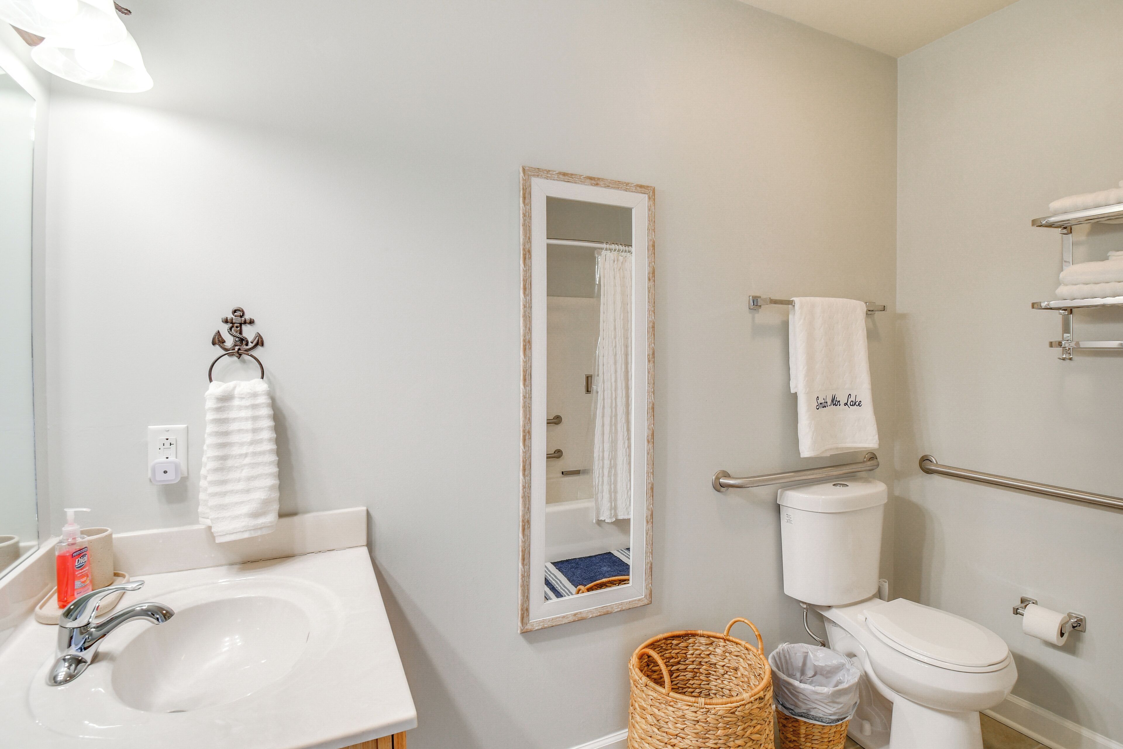 A bathroom with a sink, mirror, towel rack, toilet, and a basket.