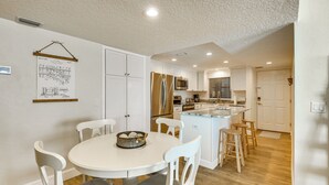 A modern kitchen with white cabinetry, a central island, and a dining area with white chairs. - Pool Access! Oceanfront Daytona Beach Shores Gem (Daytona Beach Shores)