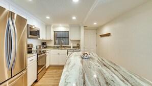A modern kitchen with stainless steel appliances, white cabinetry, and a marble countertop. - Pool Access! Oceanfront Daytona Beach Shores Gem (Daytona Beach Shores)