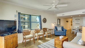 A living room with a television, wicker chairs, a blue sofa, a wooden coffee table, and a ceiling fan. - Pool Access! Oceanfront Daytona Beach Shores Gem (Daytona Beach Shores)