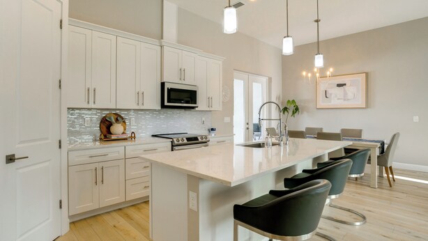 A modern kitchen with white cabinets, a large island, bar stools, and pendant lighting. - 3 Mi to Manasota Beach! Sleek Home w/ Lanai (Venice)