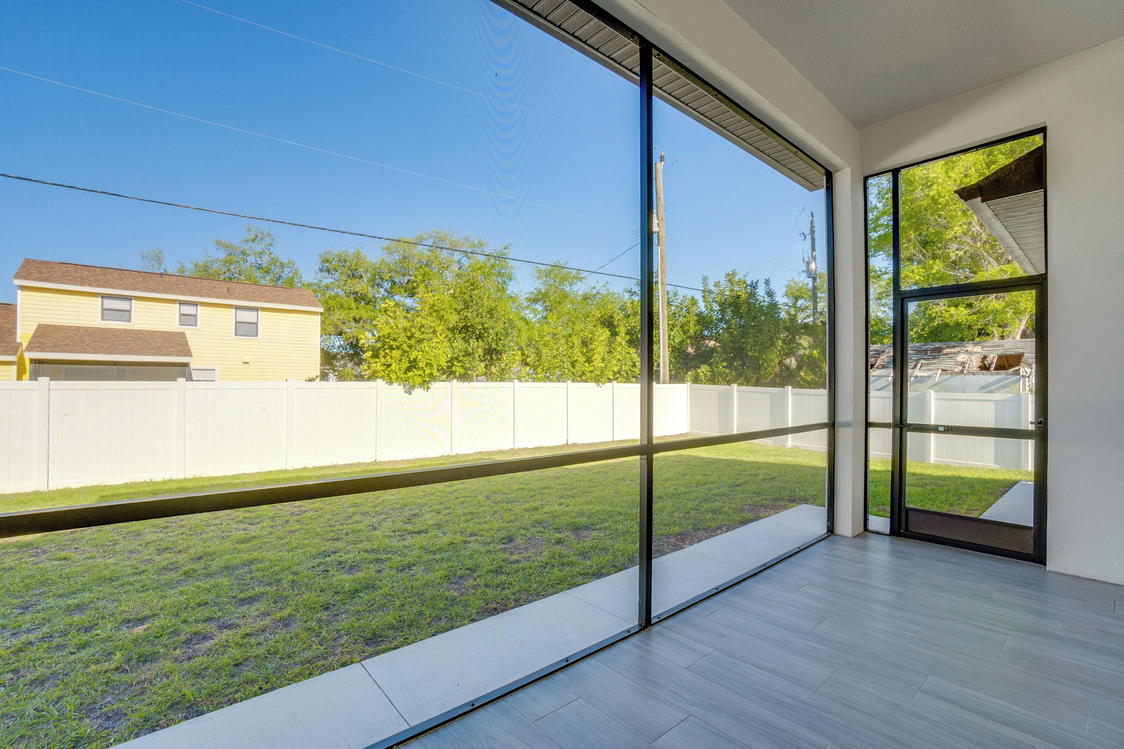 A room with large windows, a wooden floor, and a view of a fenced yard.