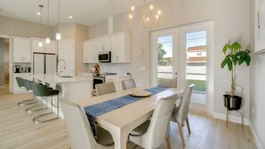 A modern kitchen with white cabinets, a central island, and a dining area with a table and chairs. - 3 Mi to Manasota Beach! Sleek Home w/ Lanai (Venice)