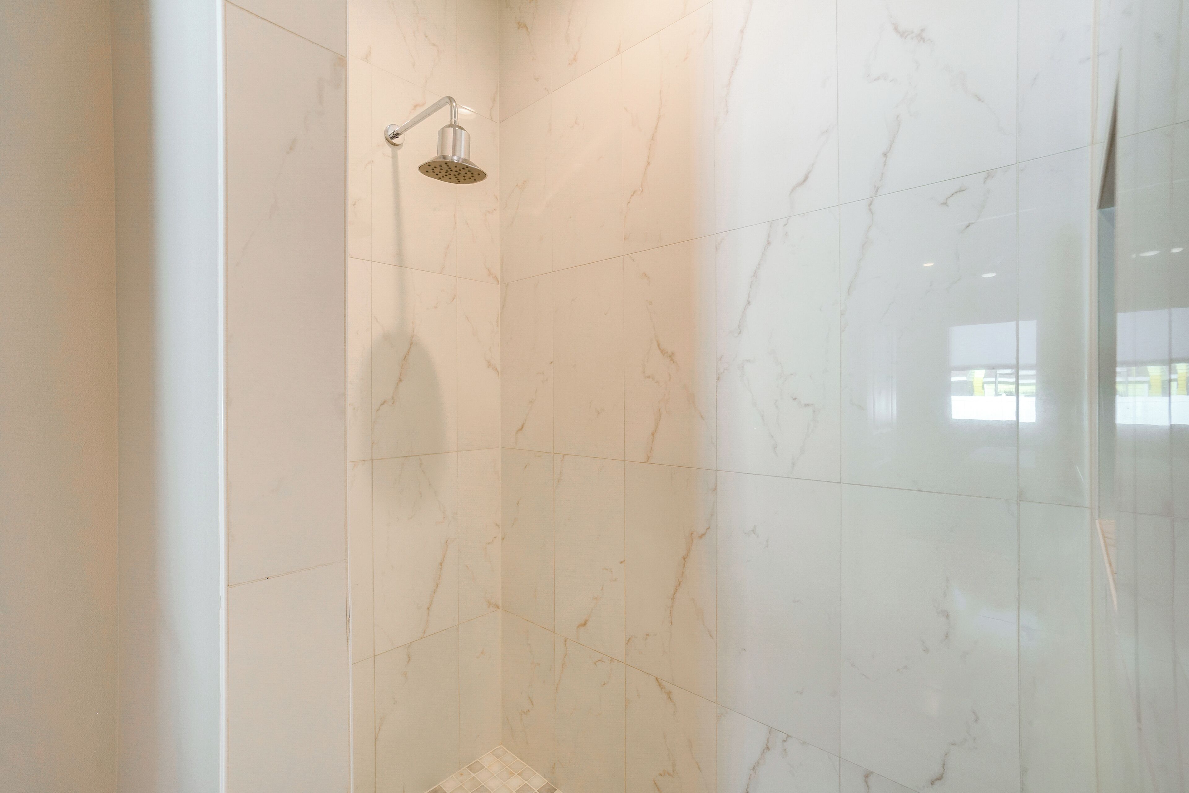 Un bagno con piastrelle in marmo bianco e un soffione.
