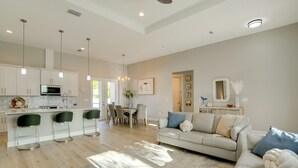 A modern kitchen with bar stools, a dining area with chairs, a sofa, and a large mirror. - 3 Mi to Manasota Beach! Sleek Home w/ Lanai (Venice)
