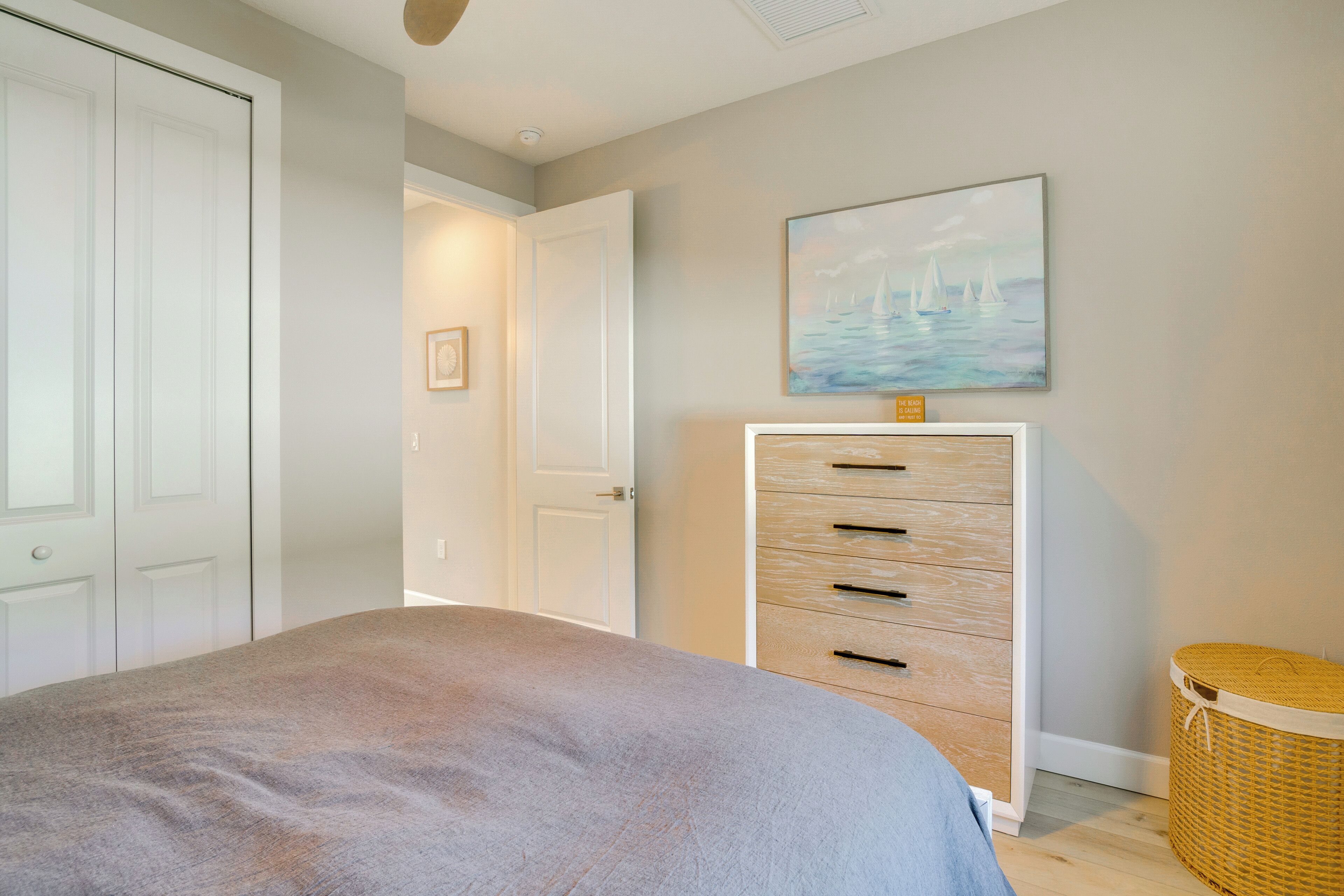 A bedroom with a bed, a dresser, a painting, and a wicker basket.