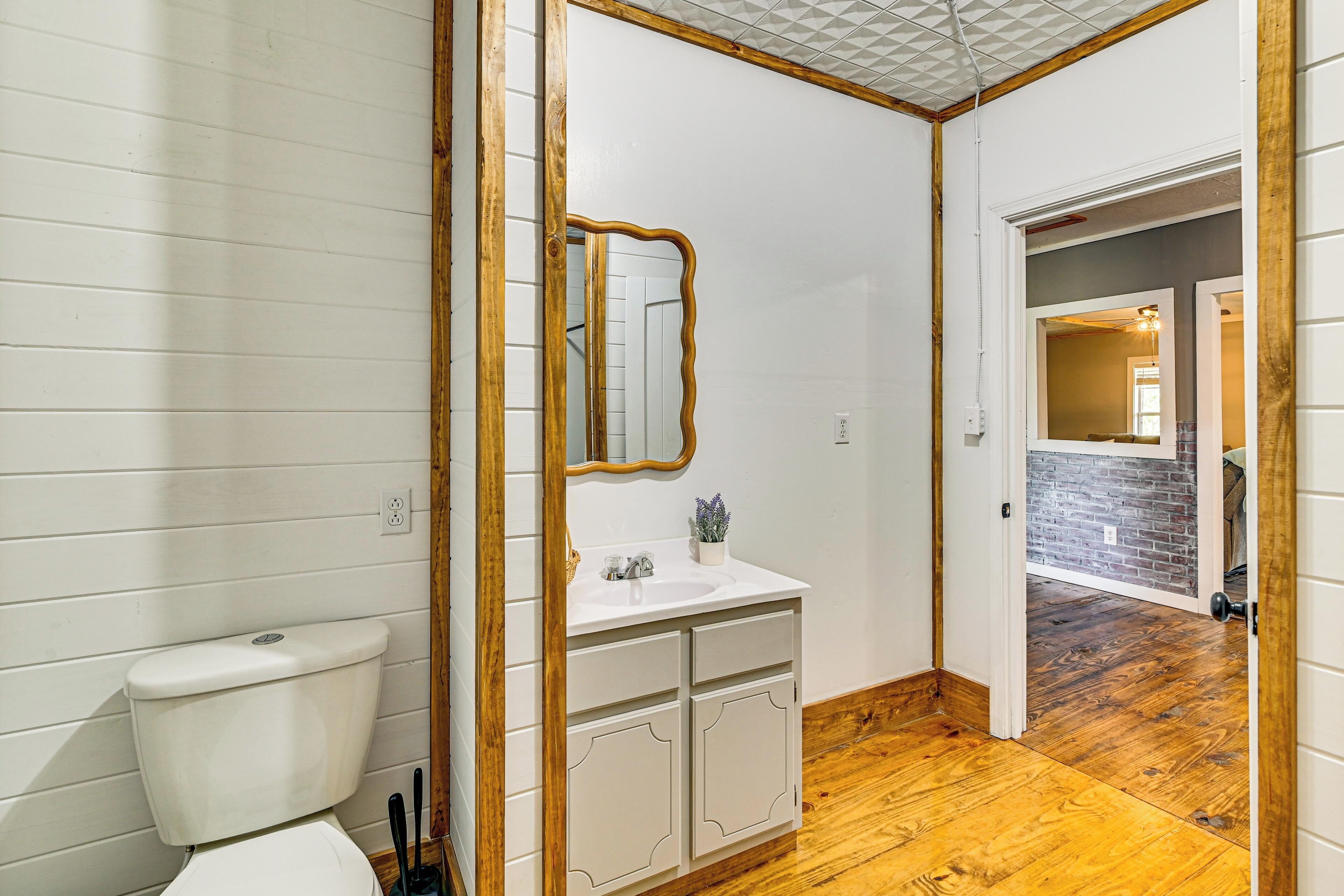 A bathroom with a toilet, sink, mirror, and wooden floor.