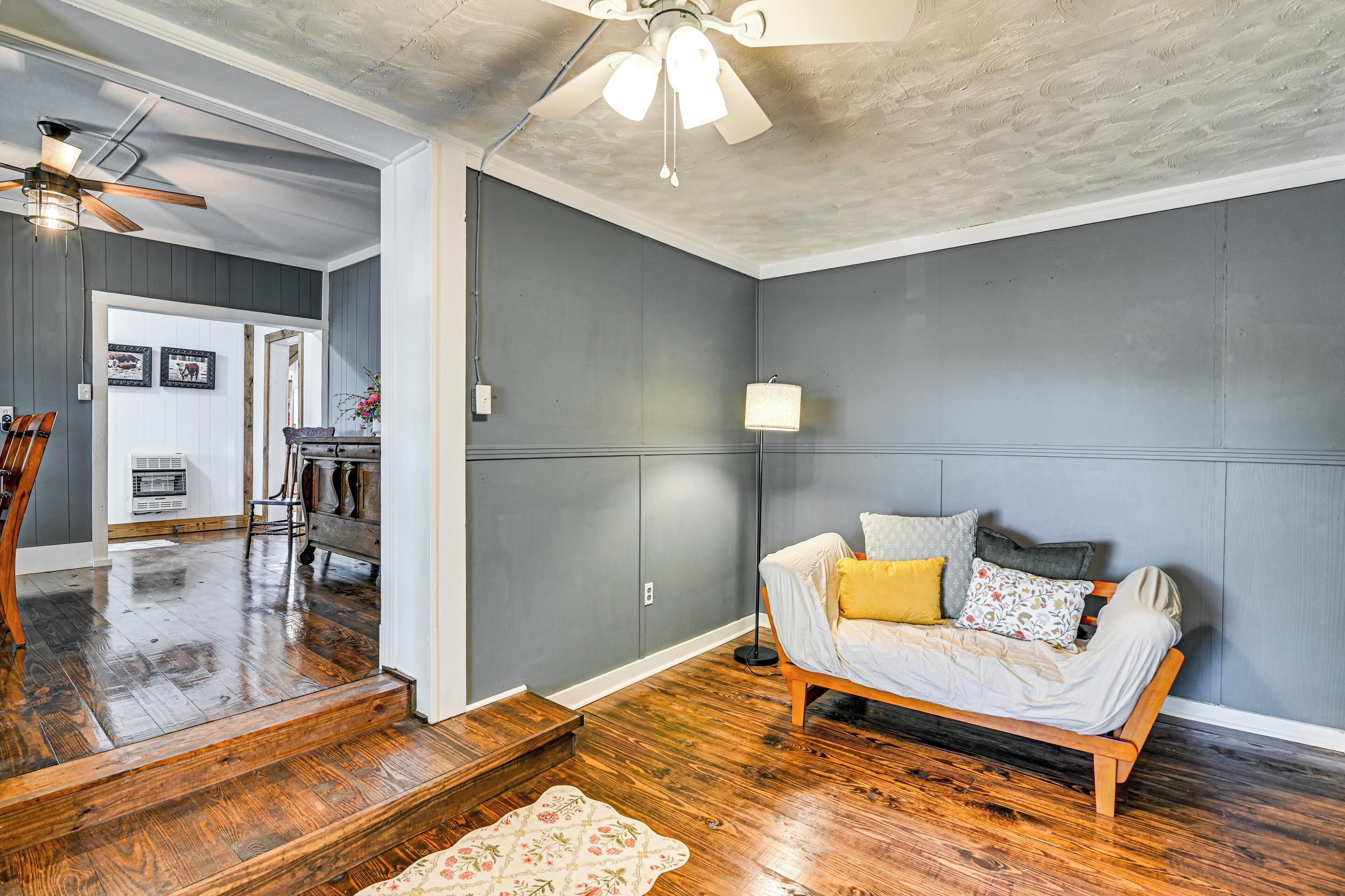 A room with a wooden floor, a sofa with cushions, a ceiling fan, and a light fixture.