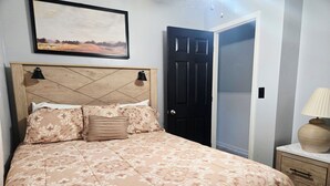 Ein Schlafzimmer mit einem Bett, einem Nachttisch, einer Lampe, einer Tür und einem Bild an der Wand.