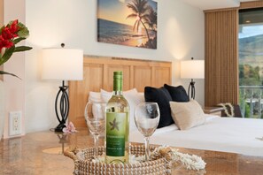 A hotel room with a bed, two bedside lamps, a wall with a sunset painting, a bottle of Starborough Sauvignon Blanc, and two glasses on a woven tray. - Mountain View Studio at Beachfront Resort in West Maui - Lahaina Shores 320 (Lahaina)