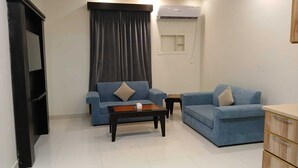 Una sala de estar con dos sofás azules, una mesa de centro, un televisor y un aire acondicionado.