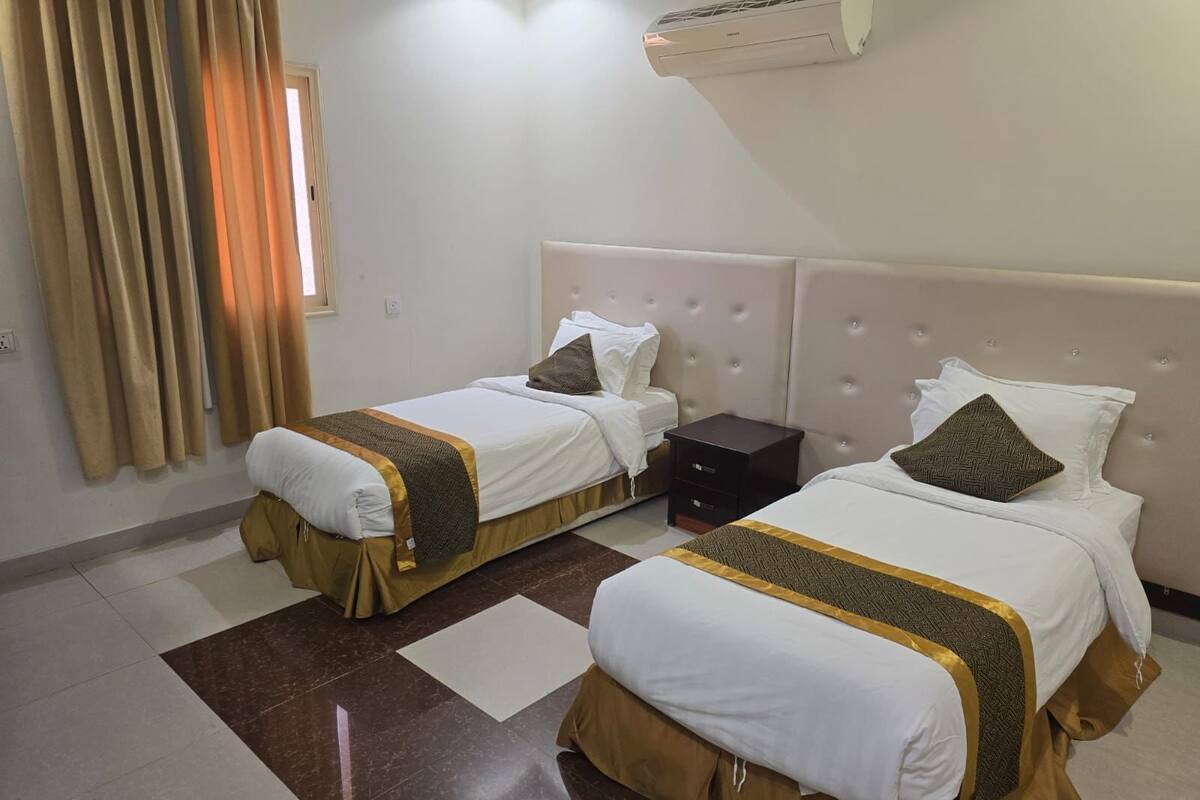 Habitación de hotel con dos camas, aire acondicionado en la pared y una ventana con cortinas.