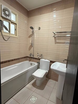 A bathroom with a bathtub, toilet, and sink, tiled walls, and a window. - Kian Allen Jizan (Jizan)