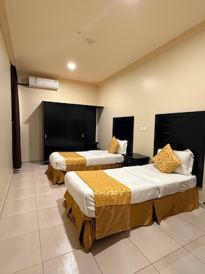 A hotel room with two beds, a wardrobe, a nightstand, and an air conditioning unit. - Kian Allen Jizan (Jizan)