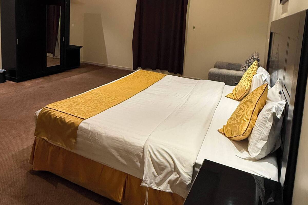 Una habitación de hotel con una cama grande, una mesita de noche, un armario y una lámpara en el techo.