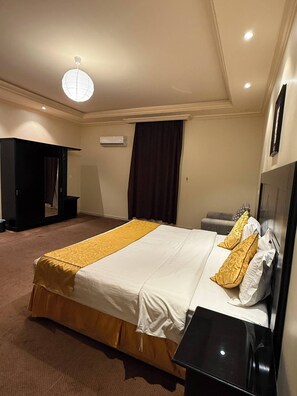 A hotel room with a large bed, a bedside table, a wardrobe, and a ceiling light. - Kian Allen Jizan (Jizan)