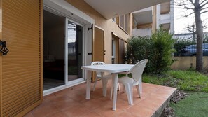 Um pátio com mesa e cadeiras, uma porta de vidro deslizante e uma pequena área de jardim.