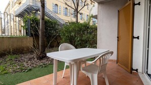 A patio with a white table and chairs, a wooden door, and a building with a staircase in the background. - Cozy apartment for 4 people with a terrace (Grasse)