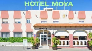 A hotel named 'HOTEL MOYA' with a distinctive architectural style, featuring a central entrance with arches and a tiled roof.