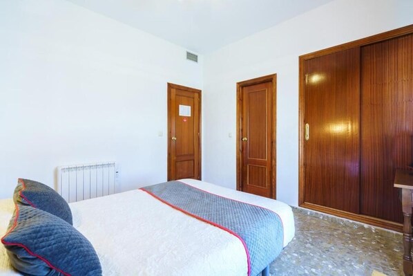 A bedroom with a bed, a radiator, and wooden doors. - Hotel Restaurante Moya (Monesterio)