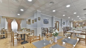 A spacious dining area with multiple tables and chairs, a ceiling with recessed lighting, and framed artwork on the walls.