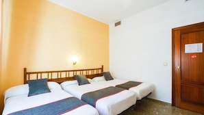 A hotel room with three beds, a wooden headboard, a wall-mounted light, and a wooden door.
