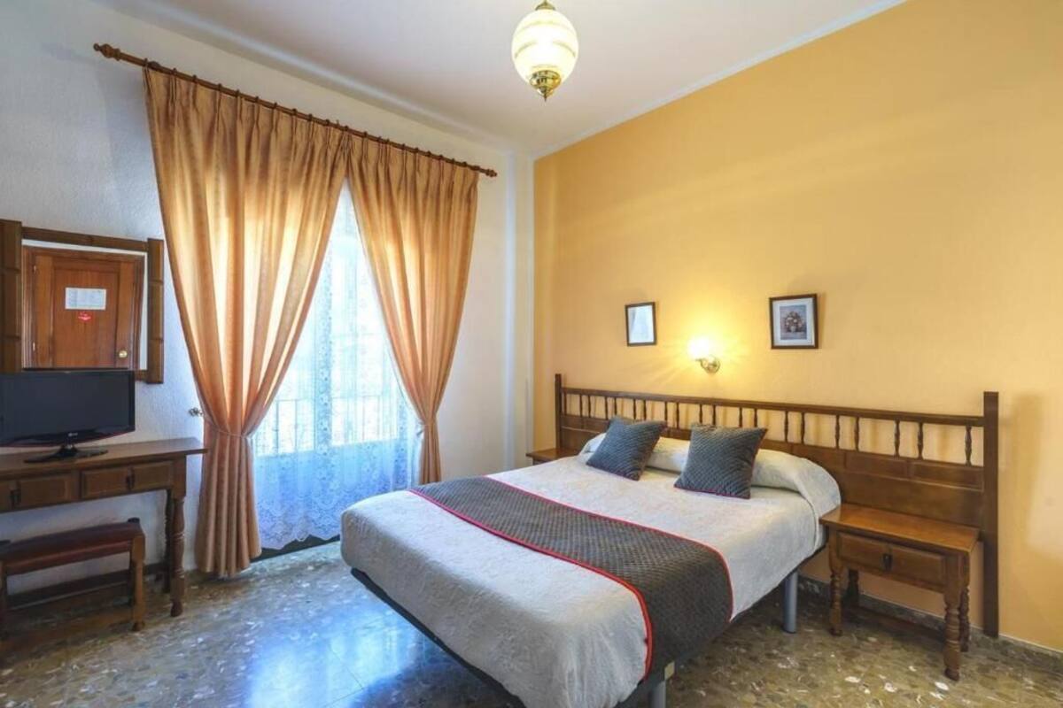 A bedroom with a bed, bedside tables, a desk with a television, and a window with curtains.
