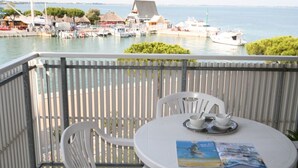 A balcony with a table, chairs, and a view of a marina with boats and buildings. - Cozy Flat With Lovely Views in Lignano (Lignano Sabbiadoro)