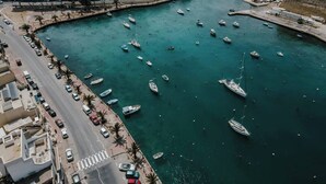 Un pueblo costero con un puerto deportivo lleno de barcos, una carretera paralela al agua y edificios a lo largo del frente marítimo.