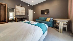 Una habitación de hotel con una cama grande, un sofá, un televisor, una mesita y un espejo.