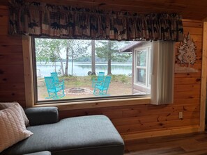 A cabin with a large window overlooking a lake, two rocking chairs, a gray sofa, and a wooden interior. - The Knotty Nook on Lost Land (Hayward)