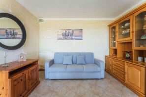 Una stanza con un divano blu chiaro, mobili in legno, uno specchio e un quadro raffigurante cavalli.
