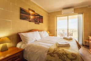 A hotel room with a bed, a nightstand with a lamp, a balcony with a view, and a painting on the wall. - Romantic Gozo Escape | Private Pool, Terrace & BBQ (Xagħra)