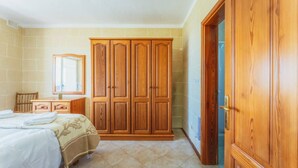 Ein Schlafzimmer mit Bett, Holzschrank und angrenzendem Badezimmer, durch eine offene Tür sichtbar.