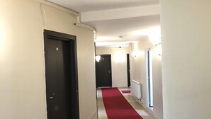 A hotel hallway with a red carpet, white walls, and black doors. - Ari Otel (Erzurum)
