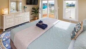 Een slaapkamer met een bed, een dressoir, een televisie, een raam en een balkon.