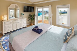 A bedroom with a bed, a dresser, a television, a window, and a balcony.