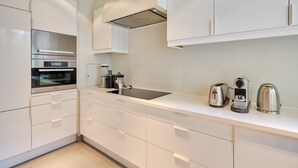 Una cocina moderna con armarios blancos, horno integrado, pileta y cafetera.