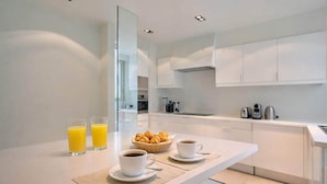 Una cocina moderna con armarios blancos, una mesa de comedor con individuales, dos tazas de café y una cesta de cruasanes.