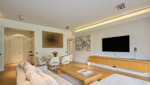 Una sala de estar moderna con sofá, mesa de centro, zona de comedor y televisor montado en la pared.