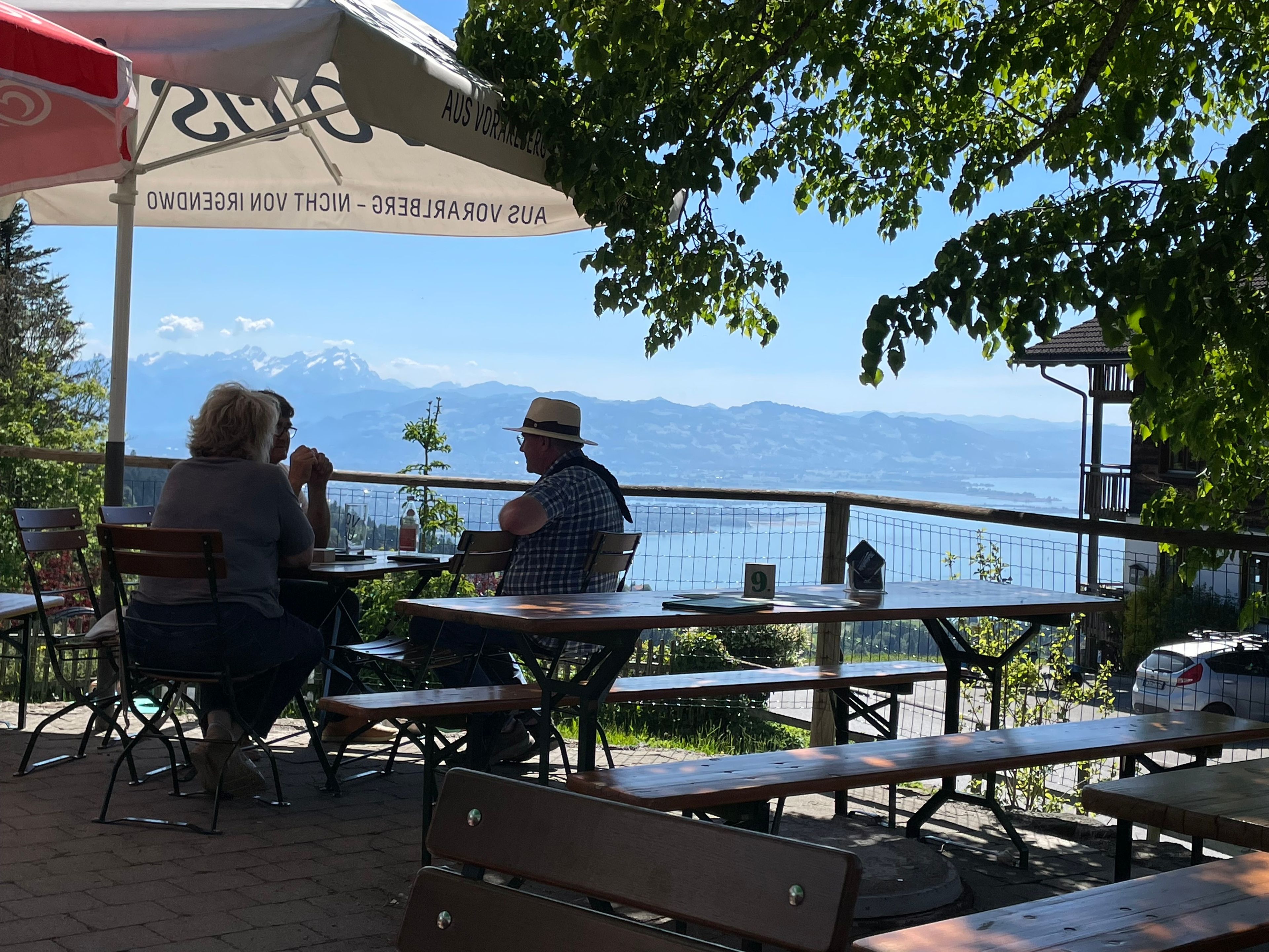 Ein Außenbereich mit Tischen und Bänken, mit Blick auf ein Gewässer und Berge.