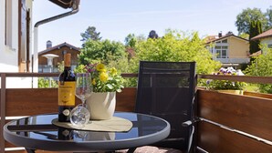 Et rundt glasbord med en vinflaske, et glas og en potteplante på en balkon.