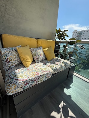 A modern sofa with patterned cushions, a yellow headboard, and a view of a cityscape through a window.
